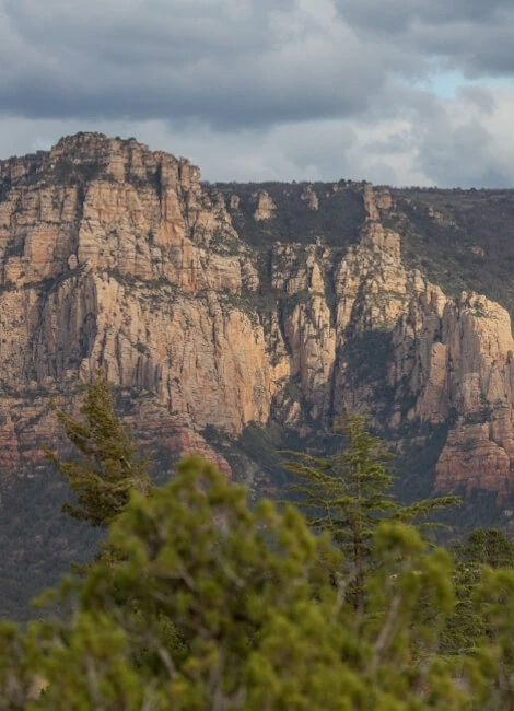 Red rock cliffs in Sedona with greenery and a cloudy sky.