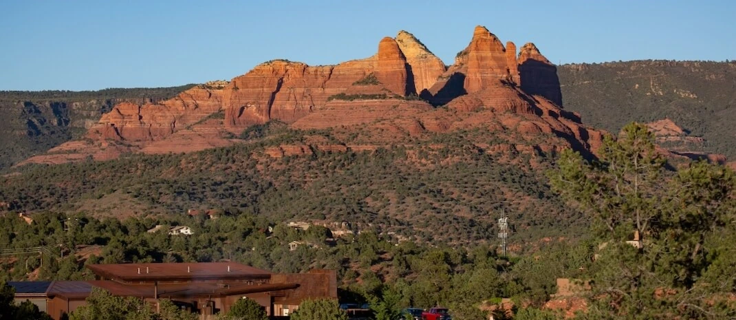 Red rock formations in Sedona, Arizona, with greenery in the foreground.