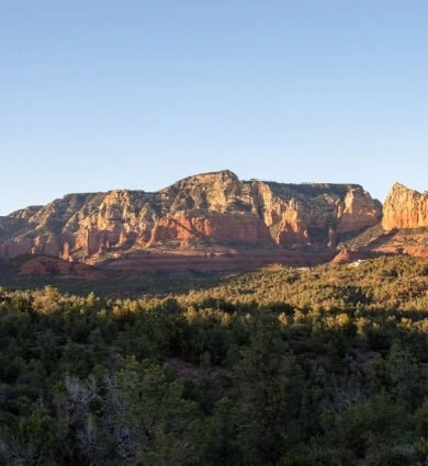 Red rock landscape in Sedona with green trees under a clear sky.