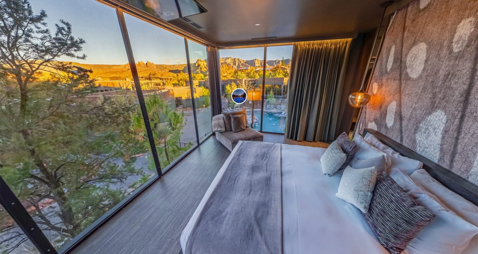 Hotel room with floor-to-ceiling windows, a bed, seating, and views of a pool, desert trees, and Sedona red rock formations.