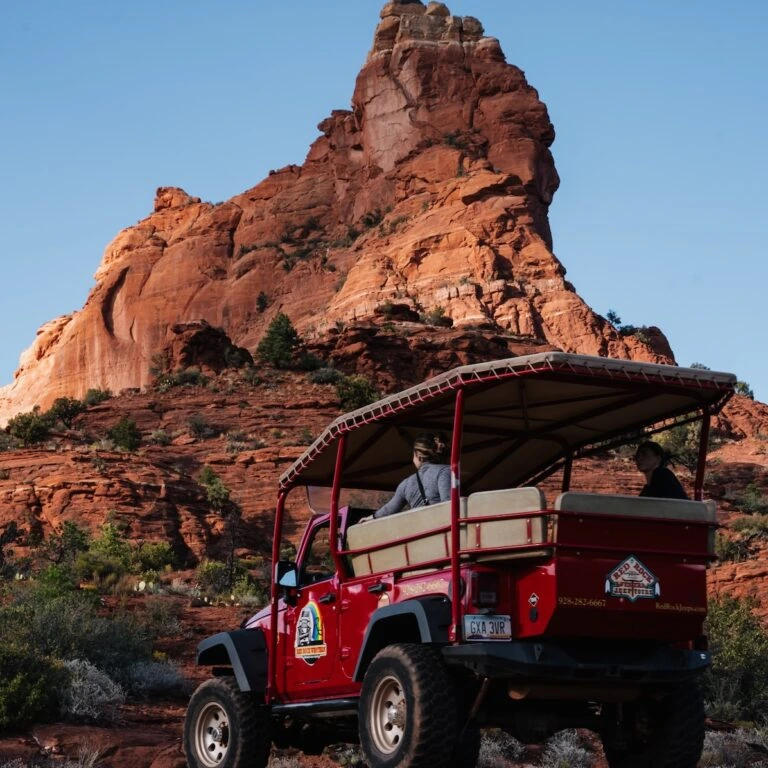 Red off-road jeep with passengers exploring Sedona’s red rock landscape under a clear blue sky.