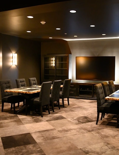 Elegant meeting room with cushioned chairs, wooden tables, and a large TV screen in dim lighting.