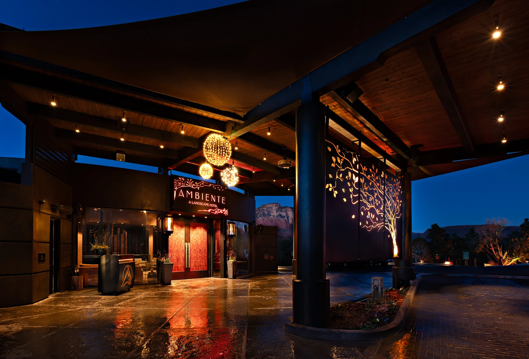 Ambiente Sedona resort entrance at night with illuminated signage, hanging lights, and decorative tree artwork on the facade.