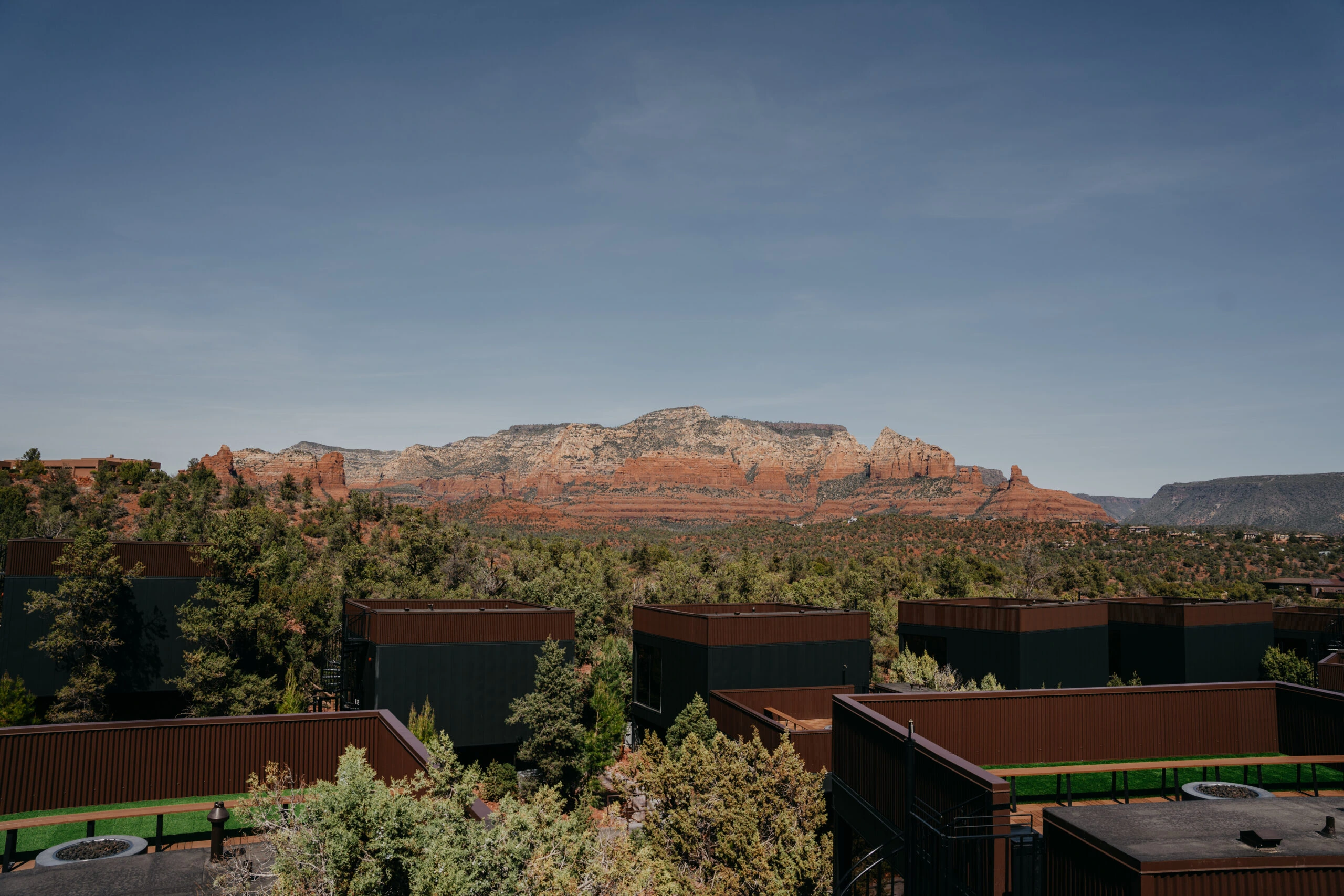 Luxury resort buildings surrounded by desert trees with Sedona's red rock formations and a clear blue sky in the background.