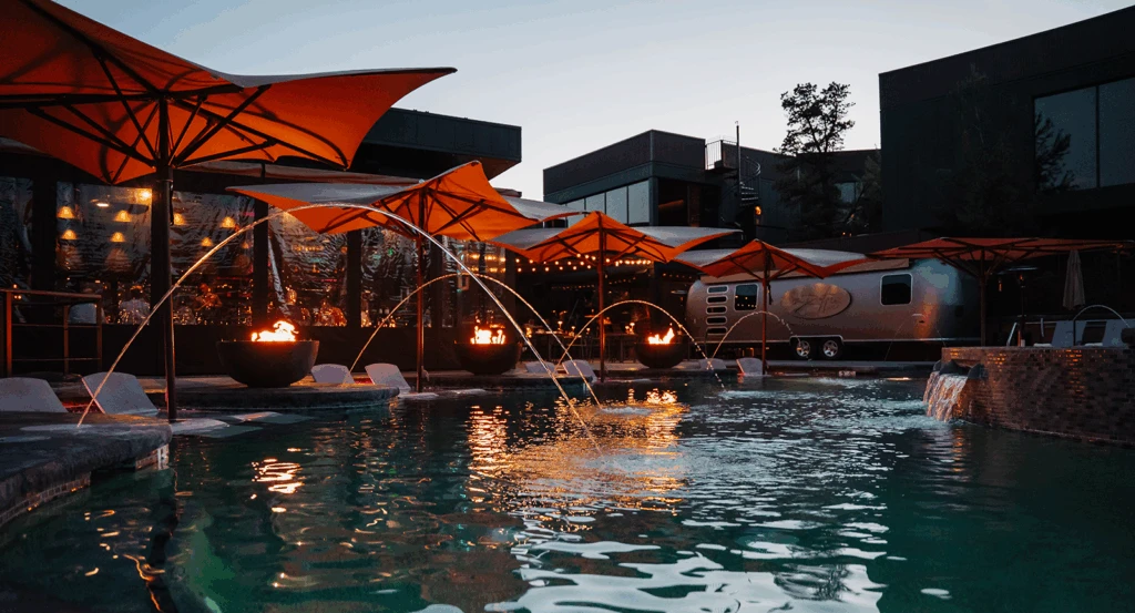 Pool at Ambiente lit up at night with firepits and orange umbrellas.
