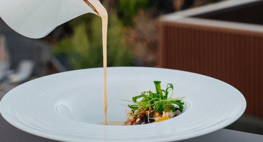 A white jar pouring sauce onto a dinner plate at Ambiente's Sedona restaurants with a view