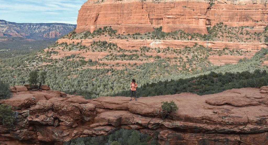 A woman on Devil's Bridge in Sedona with red rocks behind.