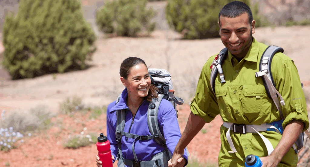 A man and a woman wearing colorful gear hiking through the desert during a Sedona couples getaway.
