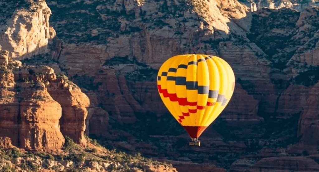 A yellow hot air balloon in front of red rock canyons
