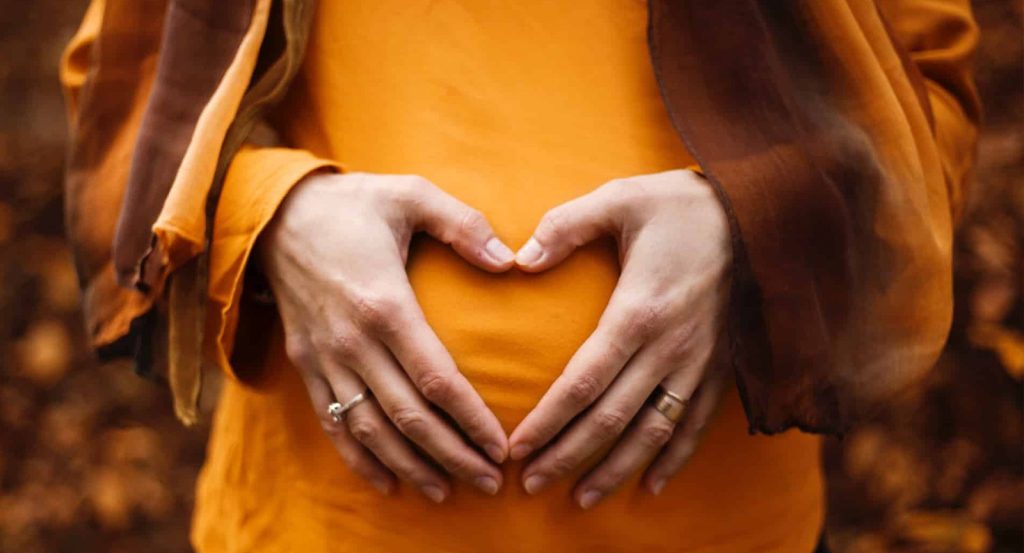 Hands making a heart shape on a pregnant belly